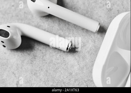White wireless earphones or headphones and plastic case or box for storage and charging on grey concrete background. Top view. Close up. Stock Photo
