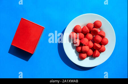 Red strawberry candies in white plate and wireless bluetooth speaker on blue background Stock Photo