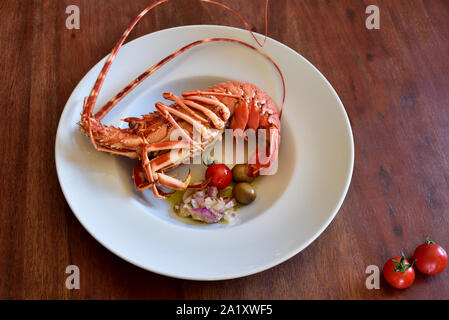 A boiled lobster lies in a white plate with side dishes on a rustic wooden table as a background Stock Photo