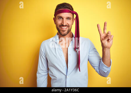 Hangover business man drunk and crazy for hangover wearing tie on head smiling with happy face winking at the camera doing victory sign. Number two. Stock Photo