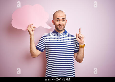 Young man holding speech bubble with blank space for message over pink isolated background surprised with an idea or question pointing finger with hap Stock Photo