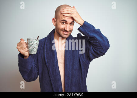 Young man wearing a bathrobe drinking a cup of coffee in the morning over isolated background stressed with hand on head, shocked with shame and surpr Stock Photo