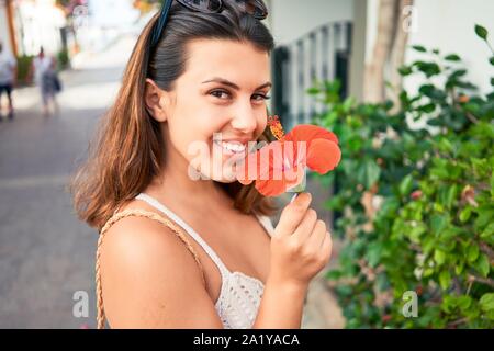 Young beautiful woman at the colorful village of Puerto de Mogan, smiling happy smelling flower on the street on summer holidays Stock Photo