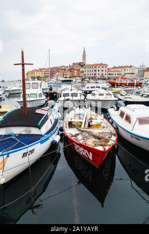 Colourful boats full of fishing equipment fill the foreground as they are moored in Rovinj harbour. Stock Photo