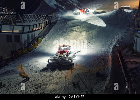 Two snowcat ratrack machines making night show performance on snow pister hill at alpine skiing resort Ischgl in Austria Stock Photo