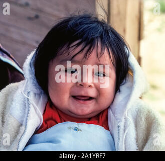 A smiling baby girl has the black hair and dark brown eyes that help identify her as a Navajo Indian, one of the Native American peoples that live in the Southwestern United States. Many of the Navajo, who are also known as Dine, live on a reservation which sprawls over 14,000 square miles of mostly arid land in Arizona and New Mexico. In addition to the Navajo (sometimes spelled Navaho), Indian tribes in the region include the Apache, and the Hopi and the Zuni. The latter two are also known as Pueblo Indians. Indian tribes often are identified as Indian Nations and each has its own culture. Stock Photo