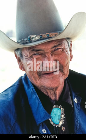 An elderly Navajo Indian man smiles from beneath his tall 'ten-gallon' cowboy hat for a portrait outdoors in the bright sunshine of southwestern Arizona, USA. His leather hatband adjorned with silver and turquoise beads competes for attention with his bolo tie that features an enormous turquoise gemstone surrounded by silver of native design. Many of the Navajo (sometimes spelled Navaho), who are Native American peoples also known as Dine, live on a reservation which sprawls over 14,000 square miles of mostly arid land in Arizona and New Mexico. Stock Photo