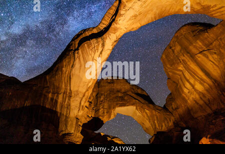 Looking up at Iconic Double Arch illuminated against a star-filled Milky Way in Arches National Park in Moab, Utah. Stock Photo