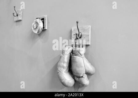 Museum of box sport. Box exhibition retro attributes. Boxing school. Final sparring. Vintage boxing gloves hang on hook wall background. Boxing gloves and ring bell. Boxing career famous sportsman. Stock Photo