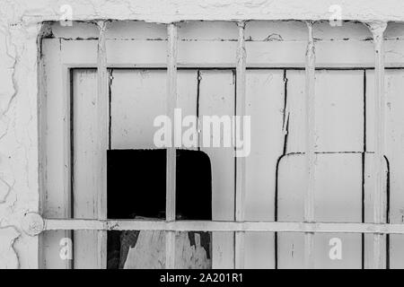 Gray grating attached over shuttered window of aged house on sunny day on town street Stock Photo