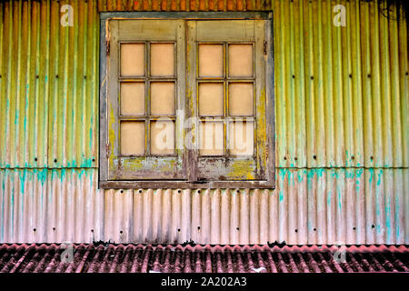 Antique window with brown wooden shutters on corrugated metal exterior of house in Geylang, Singapore Stock Photo