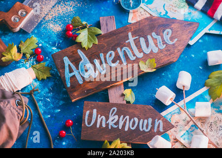 Road sign with Adventure and Unknown directions. Travel essentials creative header with socks, maps, and marshmallows, wanderlust concept Stock Photo