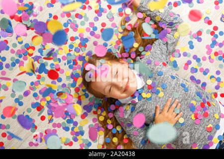Little girl lying on the floor under falling confetti. Stock Photo