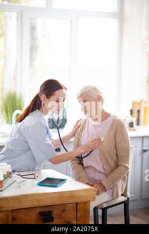 Medical attendant using stethoscope while visiting aged lady Stock Photo