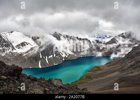 Beautiful landscape of turquoise Ala-Kul Lake in the Tien Shan mountains with white foggy clouds in Karakol national park, Kyrgyzstan