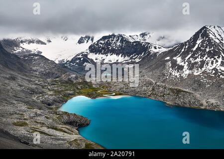 Aerial view of turquoise Ala-Kul Lake in the Tien Shan mountains with white foggy clouds in Karakol national park, Kyrgyzstan
