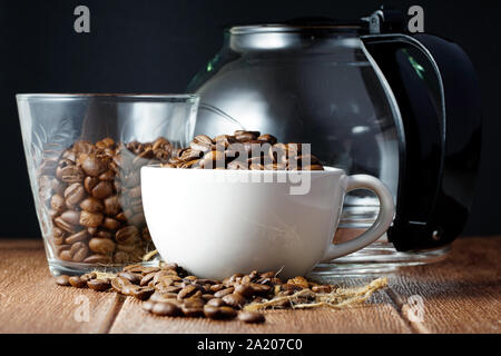 Coffee beans in a white cup  and a glass located next to coffee pot on a wooden surface Stock Photo