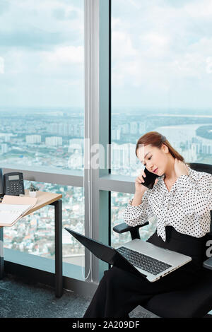 Young businesswoman massaging her stiff neck when talking on phone with client or coworker Stock Photo
