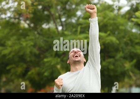 Excited happy casual man raising arm celebrating success alone in a park Stock Photo