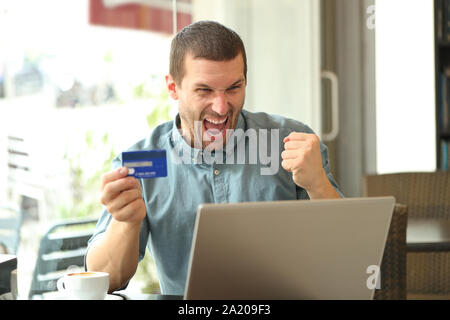 Excited man buying online with credit card and laptop sitting in a coffee shop Stock Photo