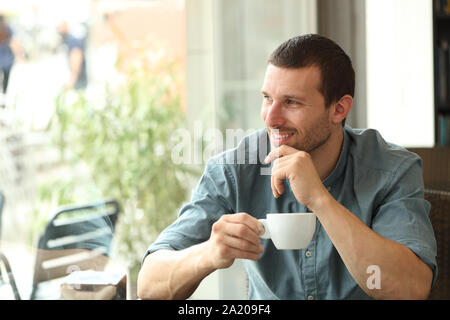Happy man holding drink cup looking away through a window sitting in a coffee shop Stock Photo