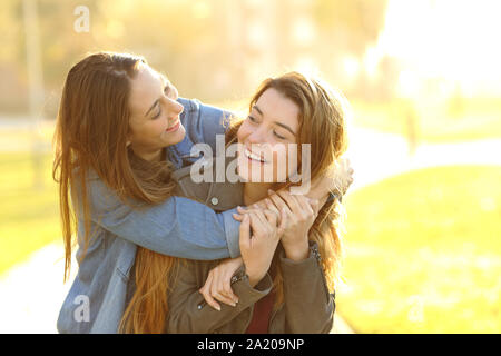 Two joyful friends joking piggybacking meeting in a park at sunset Stock Photo
