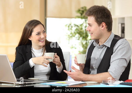Happy workers drinking coffee and talking sitting in a desk at office Stock Photo