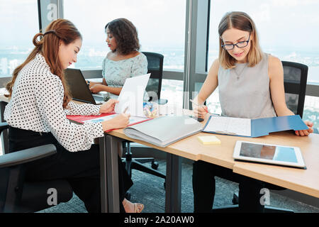 Team of female managers sitting at long office desk and examining documents with financial statistics Stock Photo