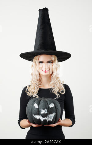 Portrait of smiling young beautiful woman in witch costume holding Halloween party decoration, isolated on white Stock Photo