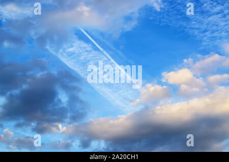 Beautiful white and gray fluffy clouds high in a blue sky. Skyscape with wide airplane trace on a day. Beauty in nature. Stock Photo
