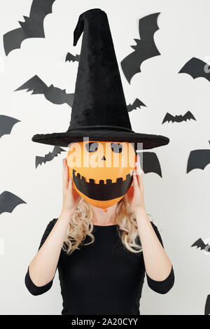 Young woman in conical hat holding orange balloon woth creepy smiling face in front of her head Stock Photo