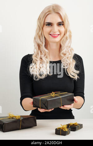 Portrait of young positive woman showing gifts she wrapped in black paper with golden ribbon Stock Photo