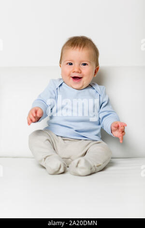 Portrait of sweet overjoyed baby boy sitting on sofa. Stock Photo