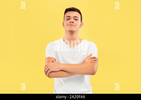 Caucasian young man's half-length portrait on yellow studio background. Beautiful male model in shirt. Concept of human emotions, facial expression, sales, ad. Standing with hands crossed. Stock Photo