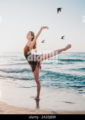 Beautiful gymnast or ballerina showing stretching on morning sea background and flying birds.Amazing scene. Nature, ballet, dance, freedom concept Stock Photo