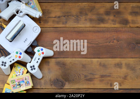 KHARKOV, UKRAINE - SEPTEMBER 18, 2019: Old 8-bit video game console and many gaming accessories like a joysticks and cartridges on wooden background. Stock Photo