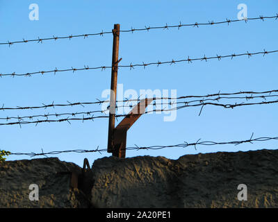 Two lines of rusty monobasic barbed wire and several lines of rusty dibasic barbed wire, stretched on rusty posts over an old concrete fence Stock Photo