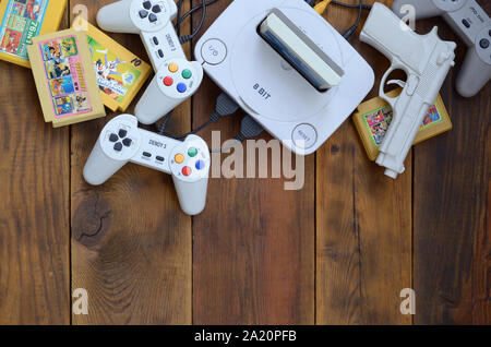 KHARKOV, UKRAINE - SEPTEMBER 18, 2019: Old 8-bit video game console and many gaming accessories like a joysticks and cartridges on wooden background. Stock Photo