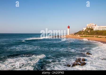 The lighthouse at umhlanga overlooked by buildings with waves breaking on the rocks Stock Photo
