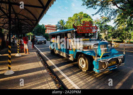 Manila, Philippines - November 10, 2018: Ordinary people wait for transport at a bus stop while blue Jeepney passes by on November 10, 2018, in Manila