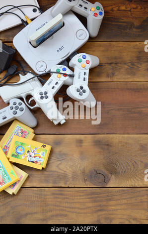 KHARKOV, UKRAINE - SEPTEMBER 18, 2019: Old 8-bit video game console and many gaming accessories like a joysticks and cartridges on wooden background. Stock Photo