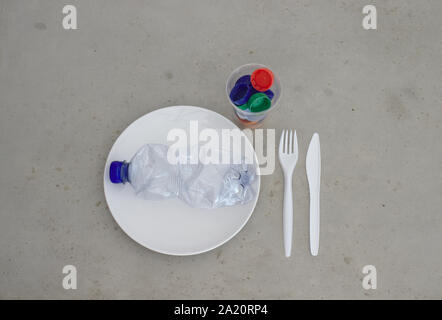 Pet plastic bottle on plate with cutlery and trash filled cup. Showing environment plastic pollution, recycling, zero waste and reusability concepts. Stock Photo
