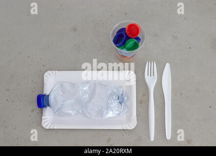 Plastic garbage on a plate, next to fork, spoon and cup filled with plastic bottle tops. Environmental pollution concept and plastic pollution. Stock Photo