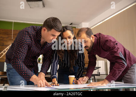 Three young and creative architects discuss the changes in the project. Modern office and blue print Stock Photo