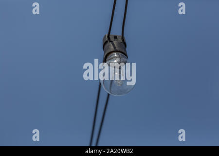View of an old incandescent lamp, wired outside on the street with blue sky background... Stock Photo