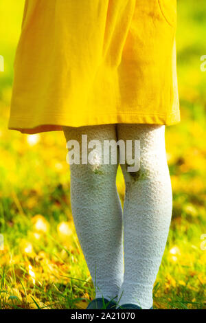 Little girl in a yellow dress and white stockings after falling to the ground. Stains of dirt on your knees. Autumn day. Dirty knees, baby Stock Photo