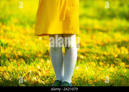 Little girl in a yellow dress and white stockings after falling to the ground. Stains of dirt on your knees. Autumn day. Dirty knees, baby Stock Photo