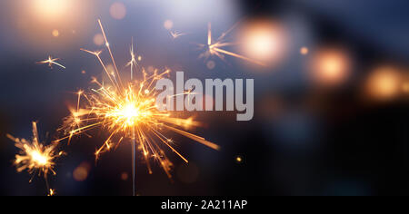 Glittering burning sparkler against blurred bokeh light background Stock Photo