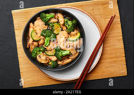 Hunan Chicken in black bowl at dark slate background. Hunan Chicken is chinese or indo-chinese cuisine takeaway dish with broccoli, zucchini, shiitake Stock Photo