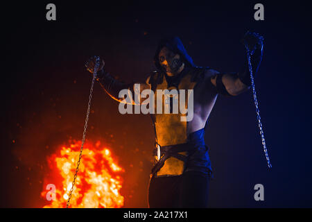 Man portraying Scorpion with chains in his hands poses at the fire background. Stock Photo